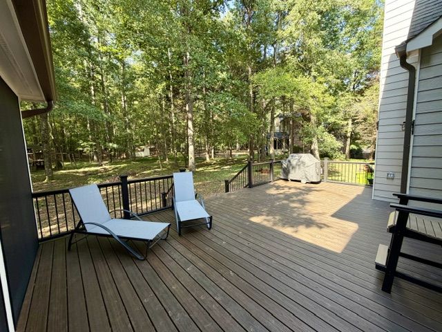 Open deck with lounge chairs, dark decking, and black railing overlooking the trees