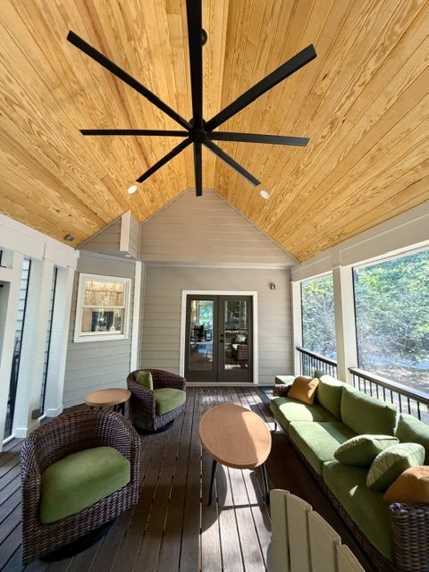 Screened porch interior with vaulted pine ceiling, black ceiling fan, and wicker seating